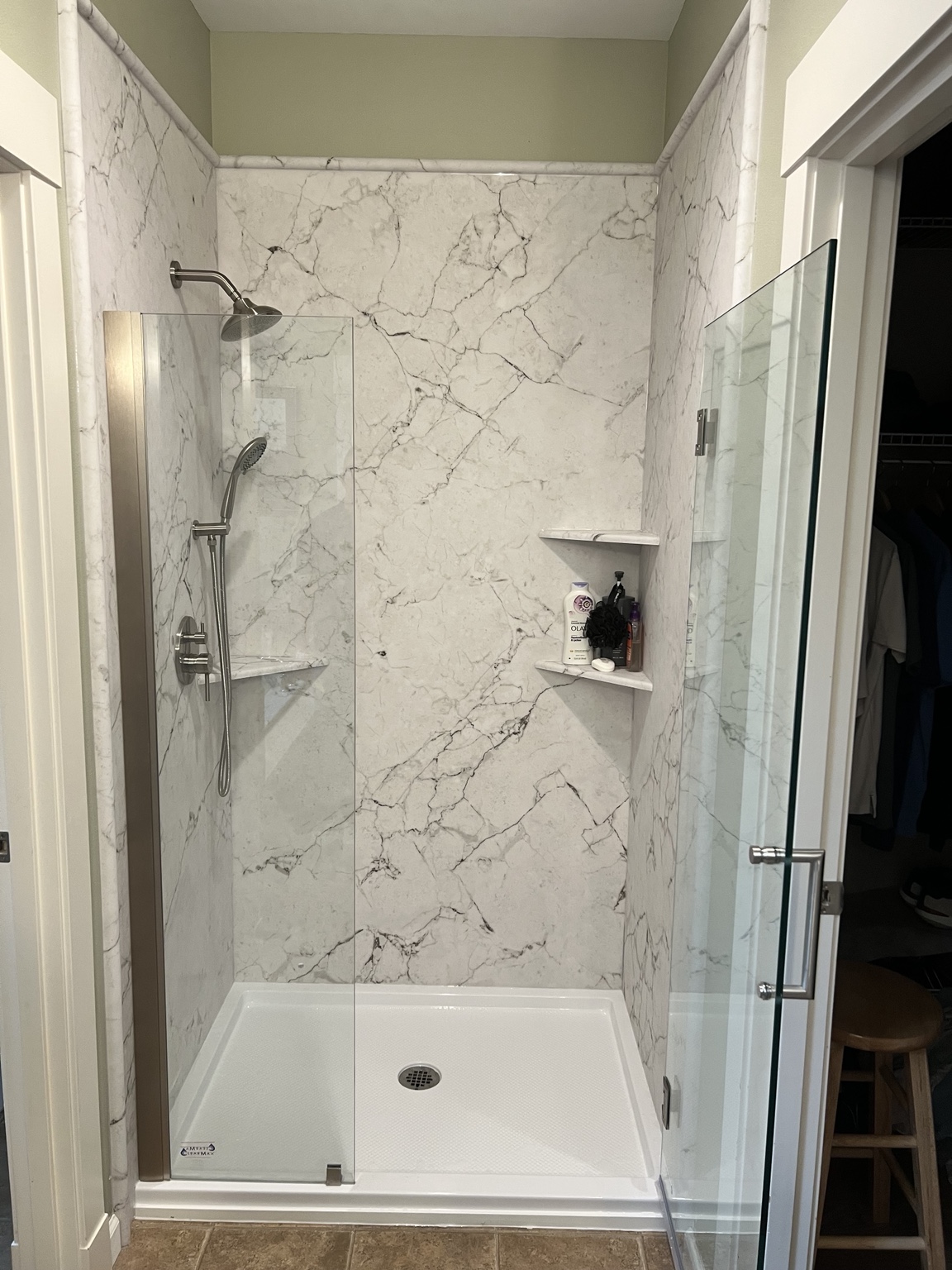 Finished Crema White Manufactured Stone shower with clear glass, a white shower base, rainfall and handheld showerheads, and matching corner shelves