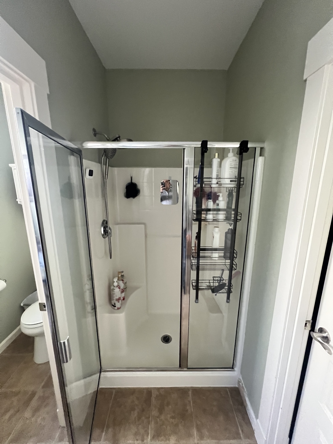Original shower with a cream-colored surround, framed glass doors, and an over-door storage rack
