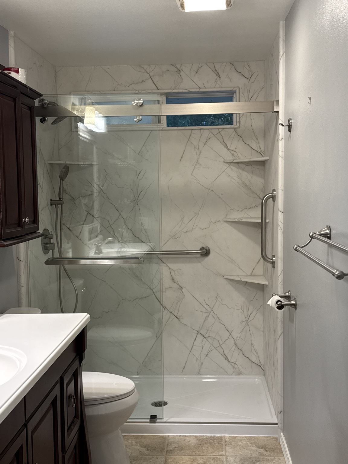 Finished low-threshold shower with marble-look walls, sliding glass, matching corner shelves, and grab bars
